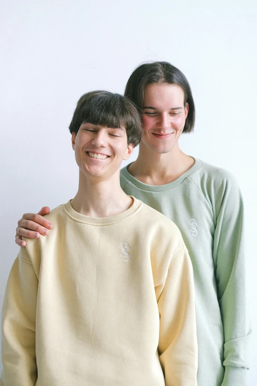 a couple of people standing next to each other, wearing a green sweater, nonbinary model, sunfaded, wearing a light shirt