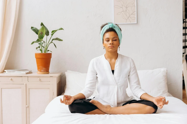 a woman sitting in a meditation position on a bed, a portrait, trending on pexels, hurufiyya, wearing a headband, white and teal garment, acupuncture treatment, calm weather