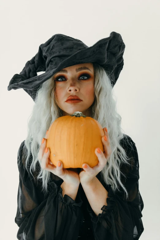 a woman in a witch costume holding a pumpkin, a photo, trending on pexels, renaissance, curled silver hair, square, gif, wears a destroyed hat