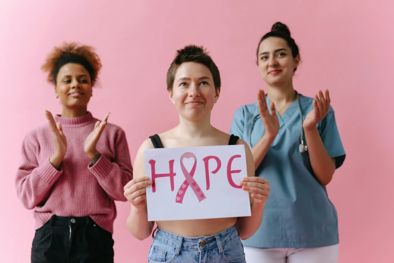 three women holding up a sign that says hope, by Emma Andijewska, trending on pexels, antipodeans, tumors, ((pink)), ribbon, various posed