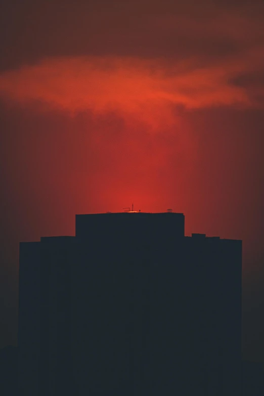 the sun is setting behind a large building, an album cover, by Attila Meszlenyi, pexels contest winner, minimalism, red cloud light, skyline, burning halo, dark tone