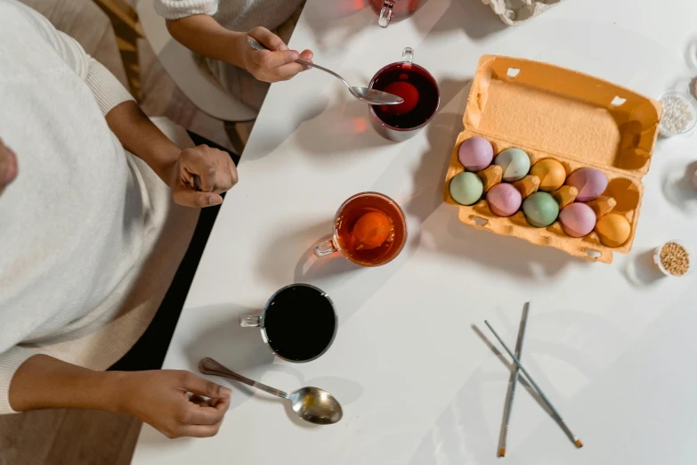 a group of people sitting around a white table, inspired by Andrea del Sarto, pexels contest winner, process art, holding easter eggs, mixing drinks, product shot, spoon placed