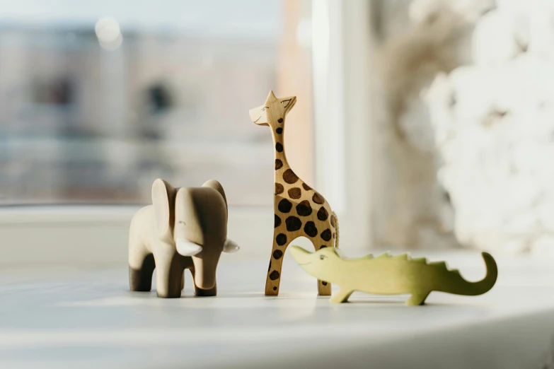 a giraffe and an elephant standing next to each other, inspired by Sarah Lucas, pexels contest winner, figuration libre, dinosaur wooden statue, vignette of windowsill, childrens toy, three animals