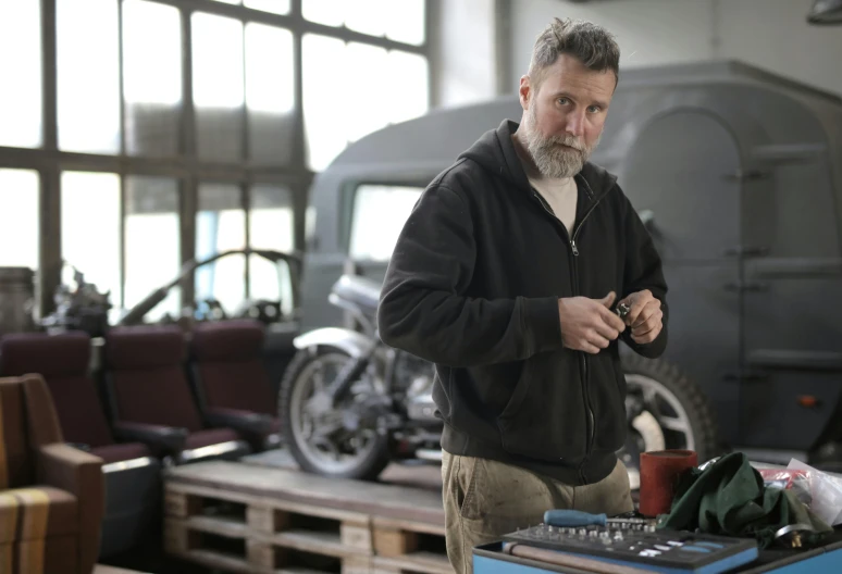 a man that is standing in front of a table, auto-destructive art, old charismatic mechanic, grey, profile image, thumbnail