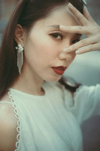 a woman in a white dress holding her hands to her face, inspired by Gao Cen, pexels contest winner, photorealism, earrings, photo taken on fujifilm superia, ethnicity : japanese, wearing an elegant outfit