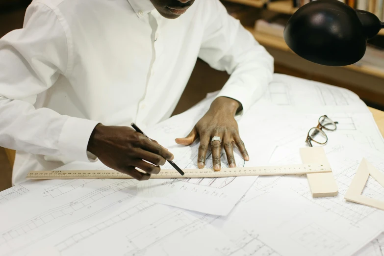 a man that is sitting at a table with a ruler, a drawing, inspired by Afewerk Tekle, pexels contest winner, luxury materials, bending down slightly, sleek hands, civil engineer