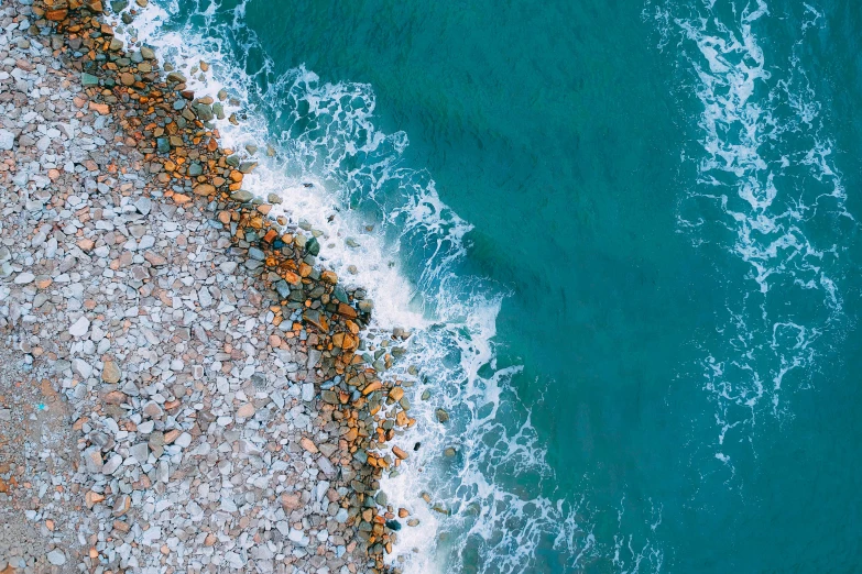 a large body of water next to a rocky shore, inspired by Andreas Gursky, pexels contest winner, cyan and orange, sea foam, top-down shot, sea spray