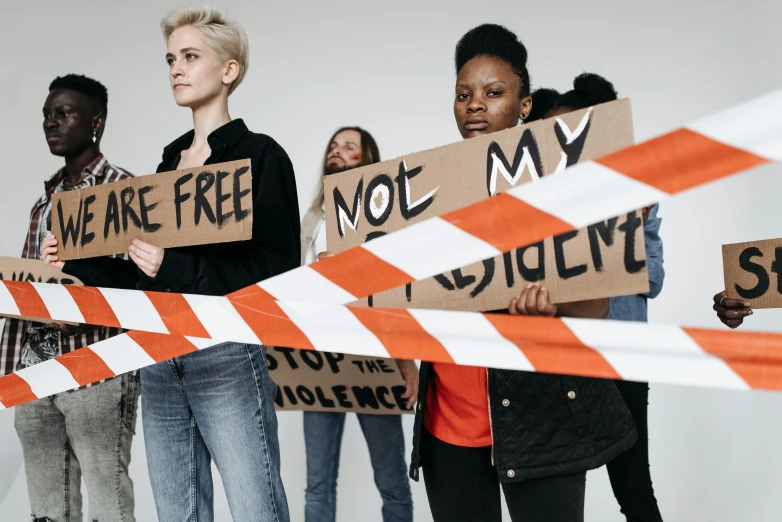a group of young people holding up signs, by Emma Andijewska, trending on pexels, police tape, woman holding another woman, brown, offwhite
