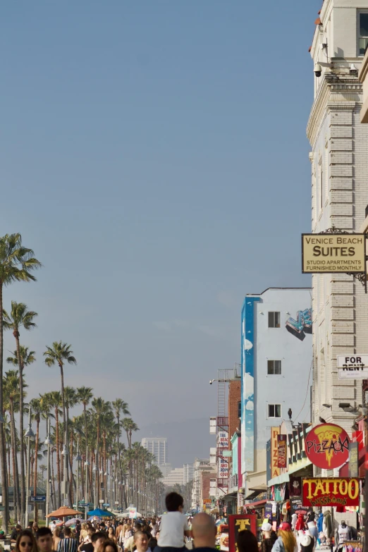 a crowd of people walking down a street next to tall buildings, renaissance, santa monica beach, hotel room, street signs, hi-res