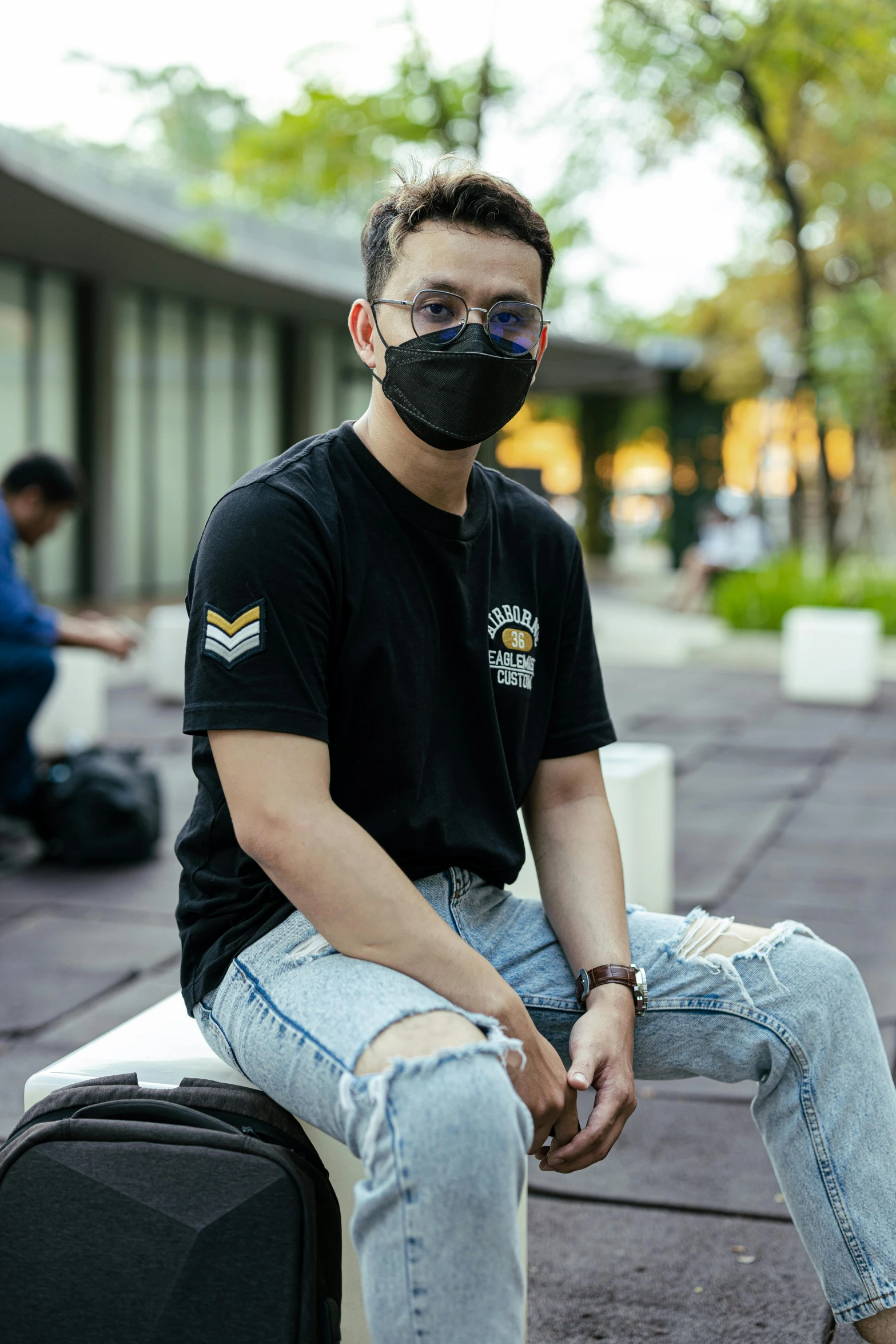 a man sitting on top of a suitcase wearing a face mask, wearing black tshirt, ramil sunga, lgbt, in a cybercity