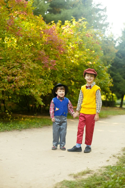 a couple of kids standing next to each other on a dirt road, inspired by Kate Greenaway, pexels, colorful uniforms, in a park, pinocchio, boys