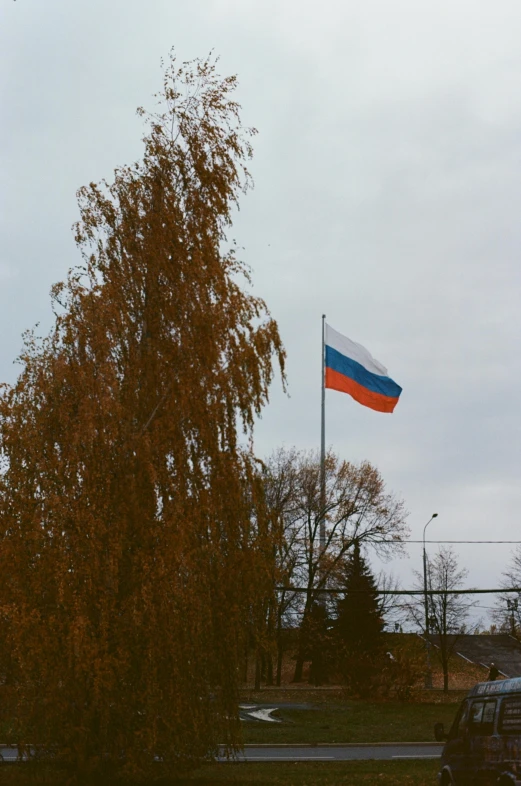 a flag flying on top of a pole next to a tree, in russia, from a distance, in the distance