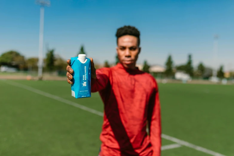 a man holding a bottle of water on a soccer field, with blue skin, cardboard, press shot, square