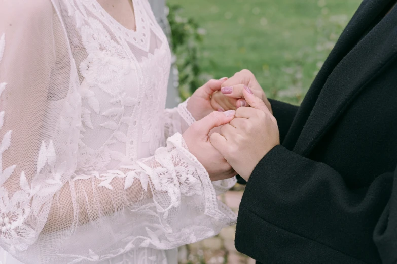 a man putting a wedding ring on a woman's finger, an album cover, trending on pexels, white lace clothing, woman holding another woman, background image, embroidered robes