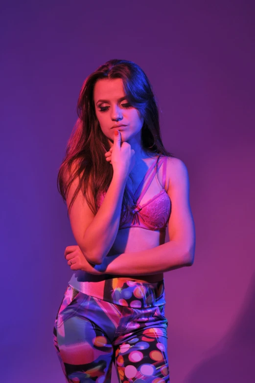 a woman standing in front of a purple background, inspired by Elsa Bleda, holography, bra and shorts streetwear, isabela moner, candid photo, concerned expression