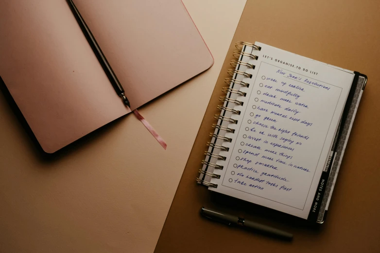 a notebook sitting on top of a table next to a pen, trending on unsplash, brown and pink color scheme, list, background image, full body image