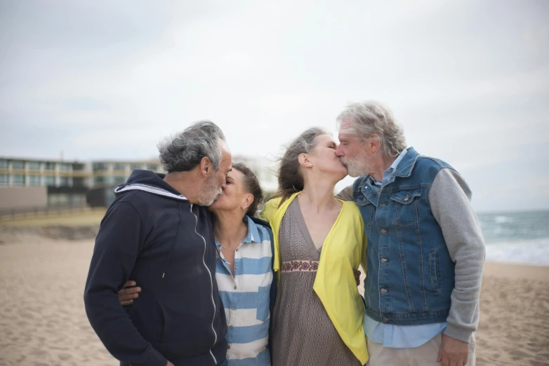 a group of people standing on top of a sandy beach, kissing, bushy white beard, 40 years old women, profile image