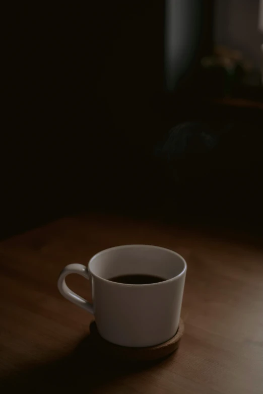 a cup of coffee sitting on top of a wooden table, in dark room, digital image