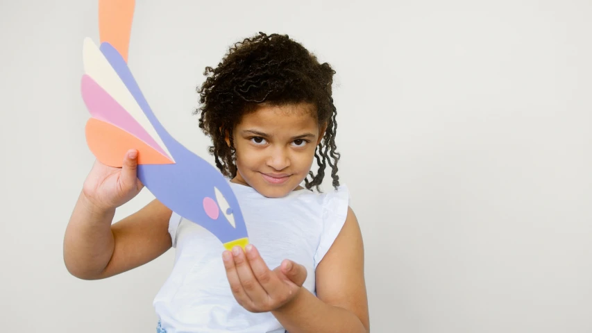 a little girl holding a paper airplane in front of her face, a child's drawing, inspired by Alexander Stirling Calder, pexels contest winner, kinetic art, light skinned african young girl, papercraft, holding a rocket, closeup of arms