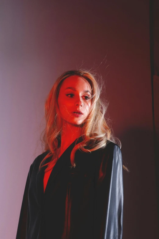 a woman standing in front of a red light, an album cover, corinne day, looking away from camera, woman in black robes, close up of a blonde woman