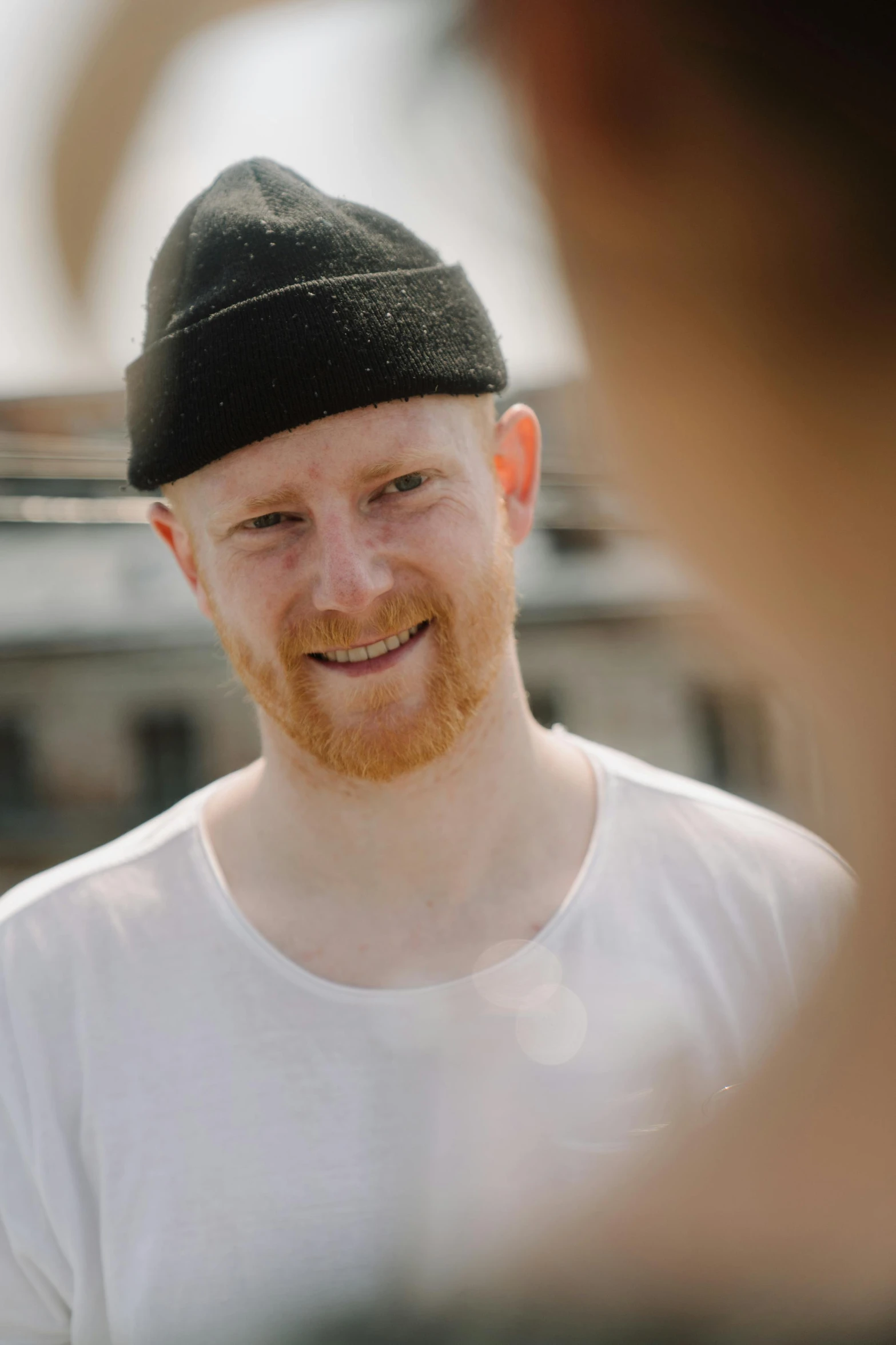 a close up of a person wearing a hat, by Daniel Seghers, ginger hair, smiling man, an all white human, he is wearing a black t-shirt