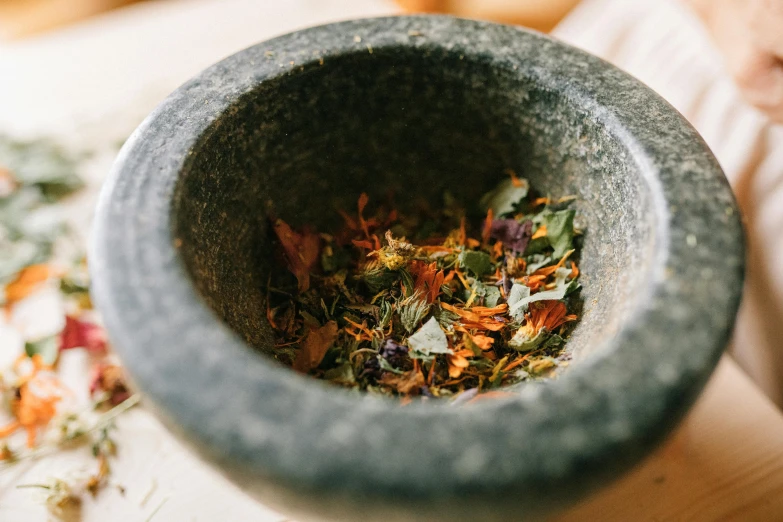 a mortar filled with herbs sitting on top of a table, trending on unsplash, dark grey and orange colours, wearing a grey robe, synthetic materials, bowl