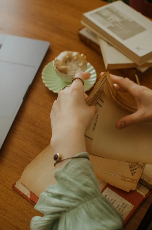 a person sitting at a table working on a laptop, a colorized photo, trending on pexels, leather jewelry, brown paper, holding books, pastry