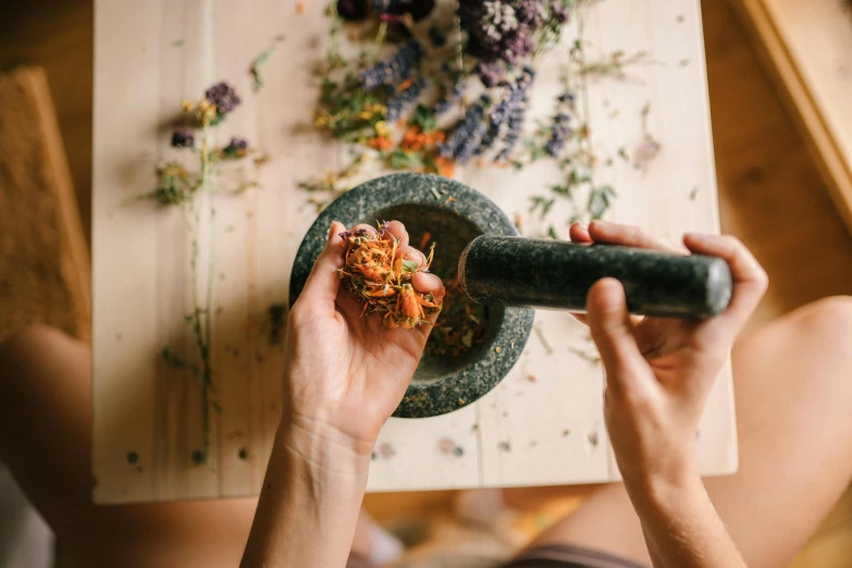 a close up of a person holding a mortar, by Julia Pishtar, trending on pexels, process art, edible flowers, ingredients on the table, herbs, spiralling