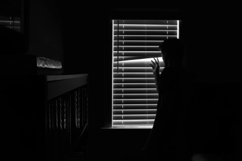 a woman standing in front of a window in the dark, a black and white photo, pexels contest winner, soft light through blinds, silhouette!!!, boy staring at the window, no lights in bedroom