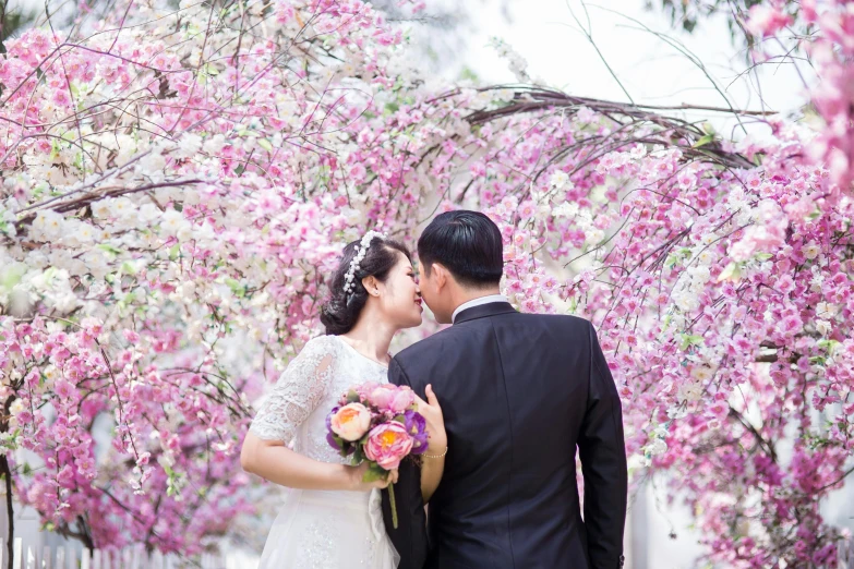 a man and a woman standing next to each other, by Nicolette Macnamara, pexels contest winner, romanticism, lush sakura, bouquet, ao dai, couple kissing