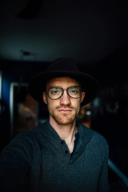 a man wearing a hat and glasses taking a selfie, unsplash, photorealism, standing in a dimly lit room, casey cooke, looking straight into the camera, james gleeson