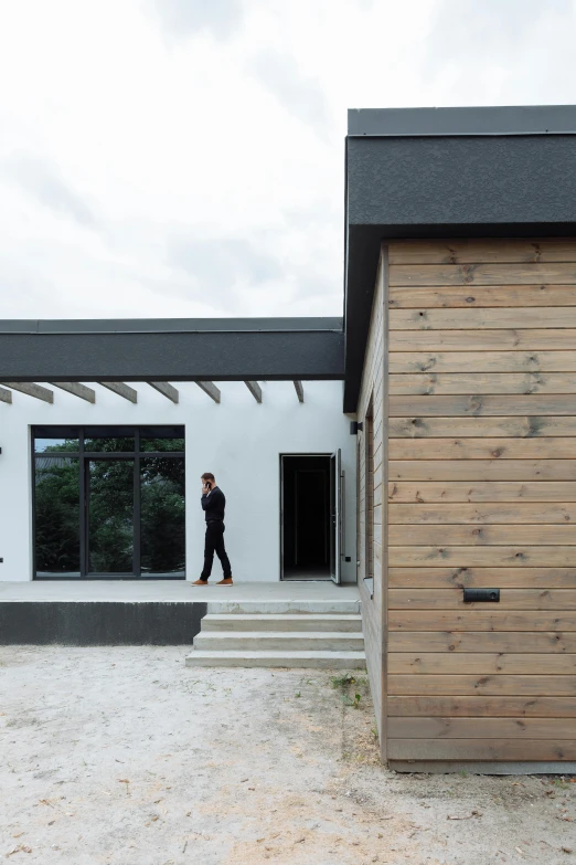 a person walking in front of a building, a portrait, inspired by Willem Claeszoon Heda, bauhaus, white plank siding, passive house, stucco walls, wide overhead shot