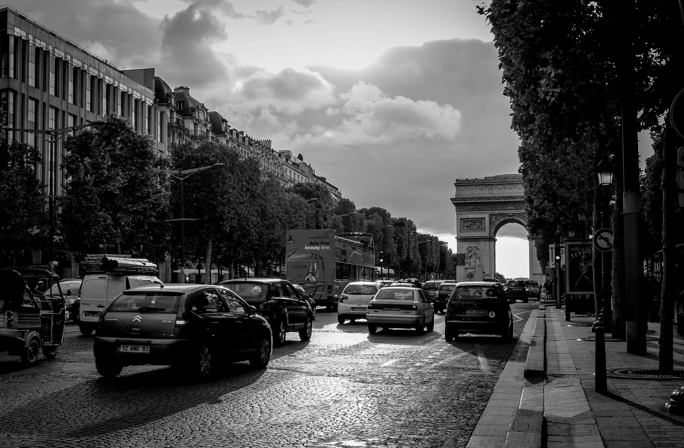a street filled with lots of traffic next to tall buildings, a black and white photo, by Etienne Delessert, unsplash, arc de triomphe full of graffiti, square, car, uploaded