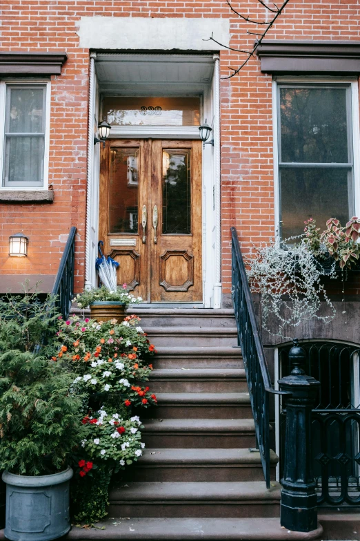 a building with a bunch of flowers in front of it, by Loren Munk, trending on unsplash, wood door, brooklyn, external staircases, late evening