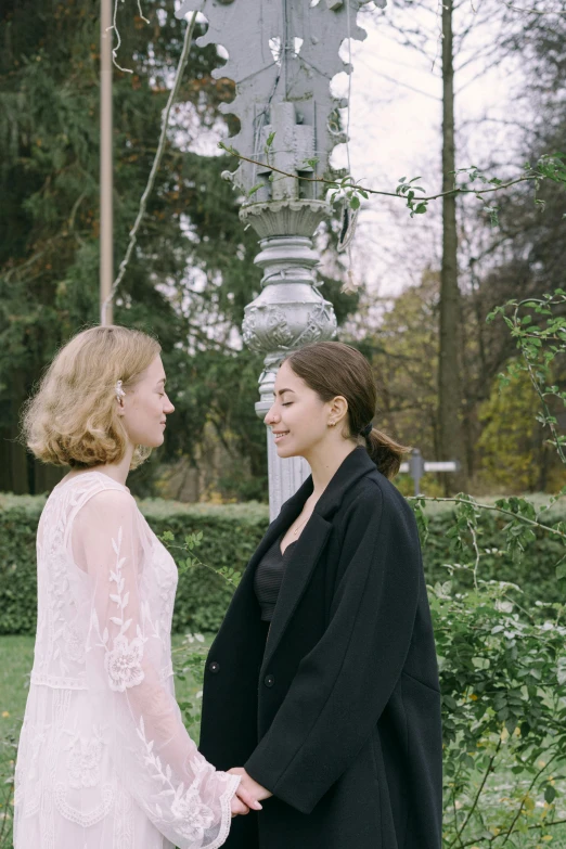 a couple of women standing next to each other, by Ulrika Pasch, unsplash, romanticism, park in background, production still, faces look at each other, low quality photo