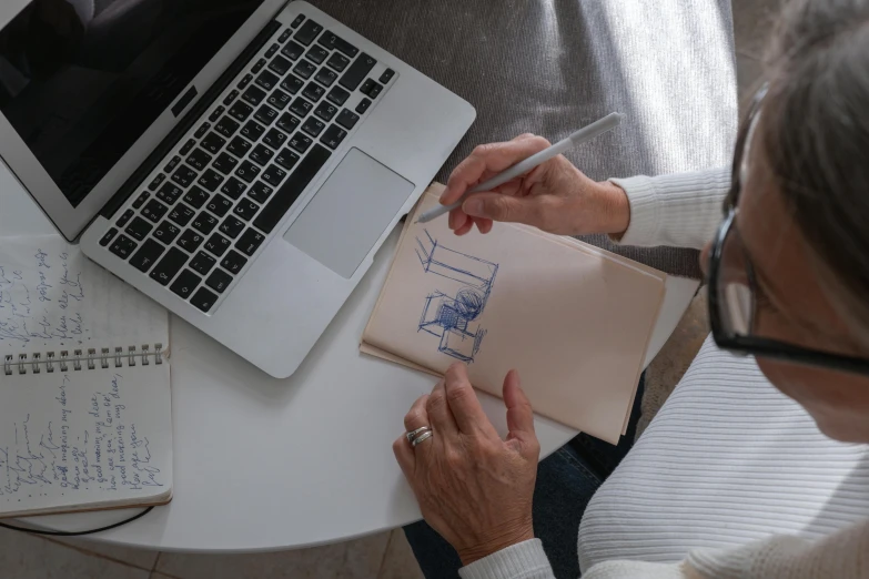 a woman sitting at a table in front of a laptop, a drawing, pexels contest winner, iconic design, top - down photograph, schematic in a notebook, a high angle shot