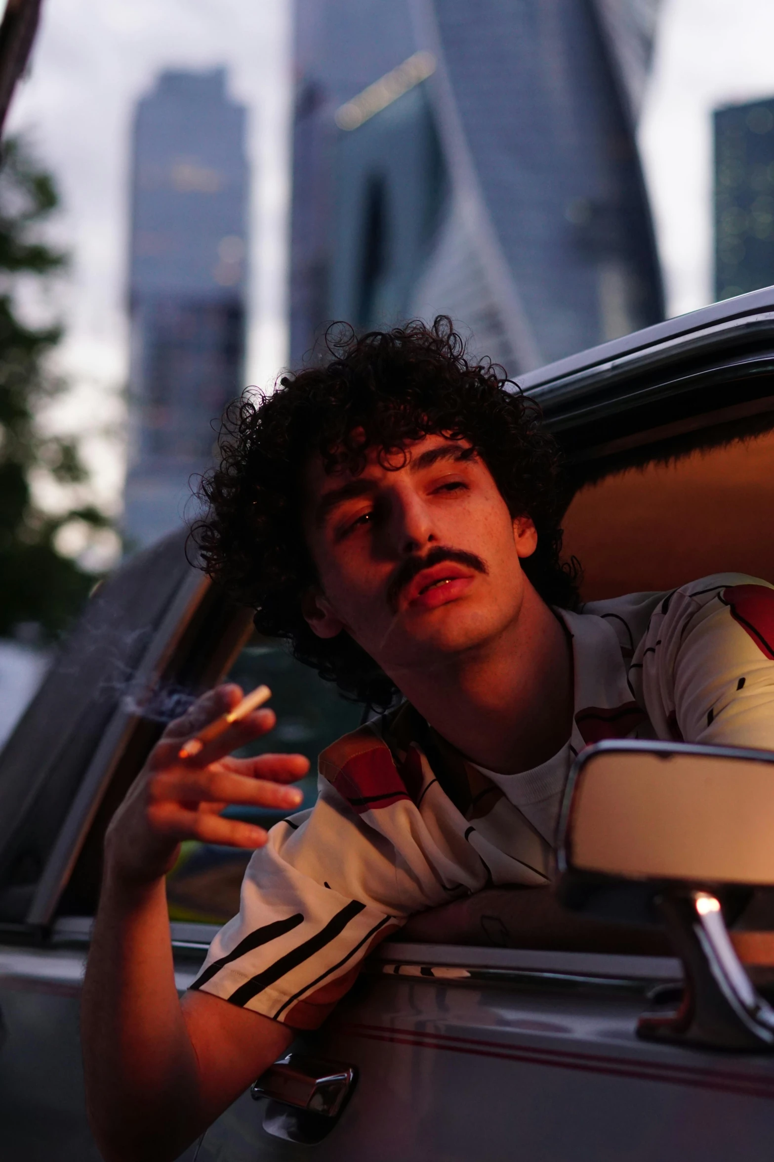 a man sitting in a car smoking a cigarette, an album cover, inspired by Nan Goldin, trending on pexels, mustache, gta in moscow, curly haired, mohamed chahin