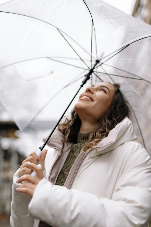 a woman holding an umbrella in the rain, trending on pexels, renaissance, wearing a white winter coat, looking upwards, smiling, wearing a turtleneck and jacket