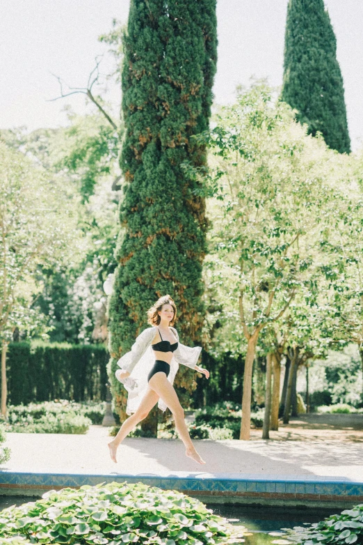 a woman running across a bridge in a park, inspired by Luis Paret y Alcazar, unsplash, arabesque, white high waisted swimsuit, vintage photo, in a verdant garden, miranda kerr