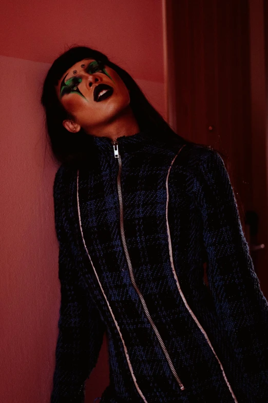 a woman with makeup on her face leaning against a wall, an album cover, inspired by Elsa Bleda, trending on pexels, graffiti, tartan hoodie, ( ( dark skin ) ), darkwave goth aesthetic, with mouth open