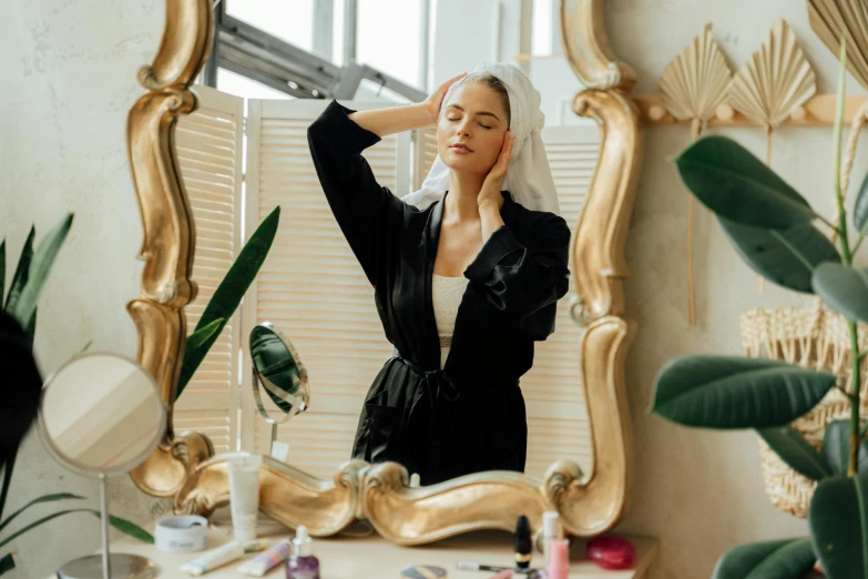 a woman that is standing in front of a mirror, trending on pexels, renaissance, photoshoot for skincare brand, golden halo behind her head, wearing a black robe, on a white table