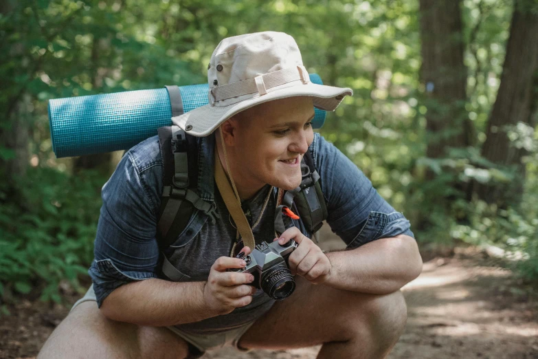 a man squatting down while holding a camera, by Meredith Dillman, wearing a travel hat, avatar image, camp, high quality image