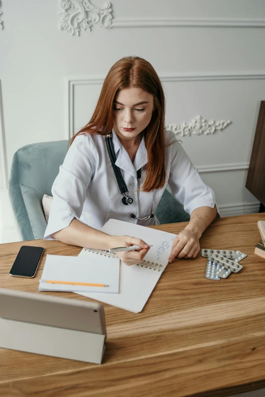 a woman sitting at a desk in front of a laptop, medicine, pen and paper, curated collections, post graduate