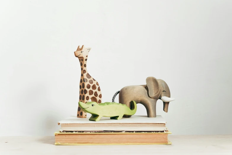 a giraffe, an elephant and a crocodile on a stack of books, inspired by Sarah Lucas, trending on unsplash, new sculpture, wooden art toys, story book, high resolution product photo, mid-30s