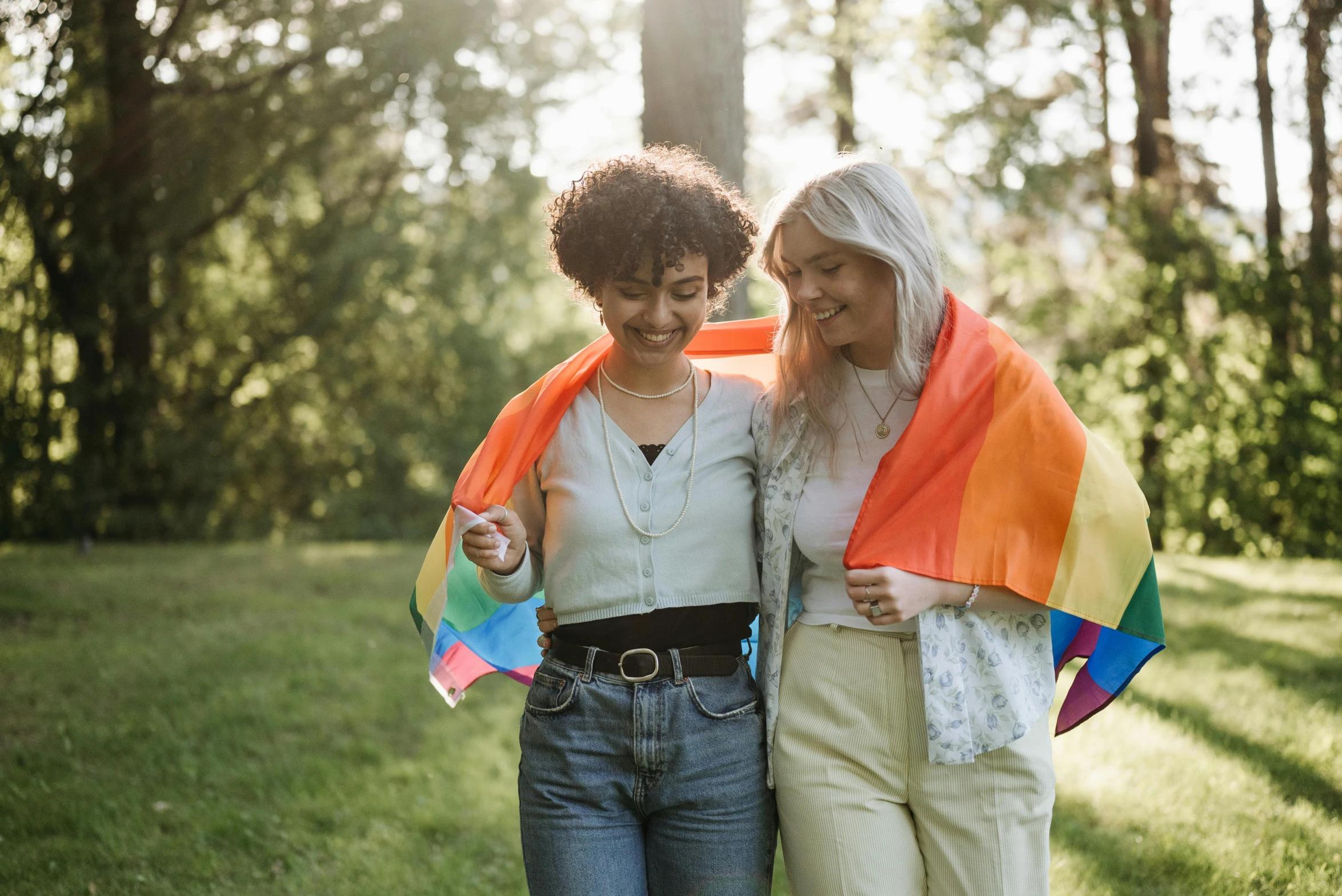 a couple of women standing next to each other, trending on pexels, lgbt flag, walking at the park, charli bowater and artgeem, a wooden