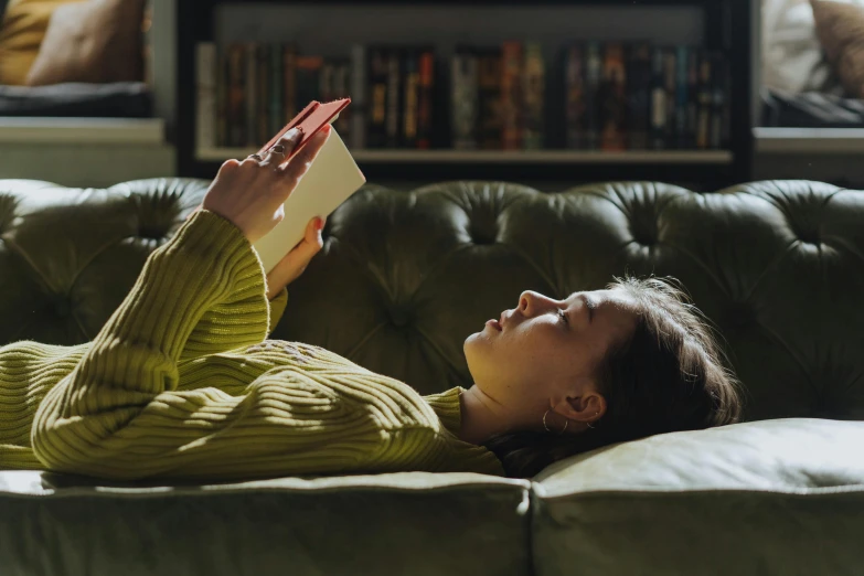 a woman laying on a couch reading a book, a portrait, trending on pexels, wearing a green sweater, dwell, vhs, instagram photo