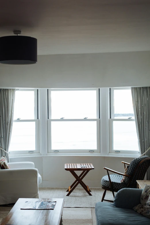 a living room filled with furniture and a flat screen tv, by David Donaldson, unsplash, light and space, bay window, calm seas, curtains, panorama shot