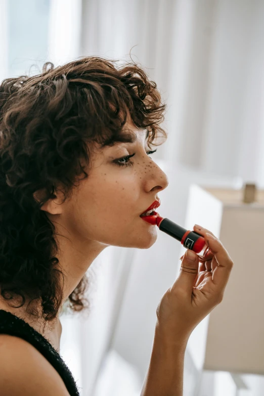 a woman putting on lipstick in front of a mirror, trending on pexels, curly brown hair, it has a red and black paint, promo image, sharpie