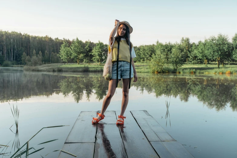 a woman standing on a dock next to a lake, by Julia Pishtar, pexels contest winner, hurufiyya, wearing shorts and t shirt, wearing farm clothes, avatar image, alexey gurylev