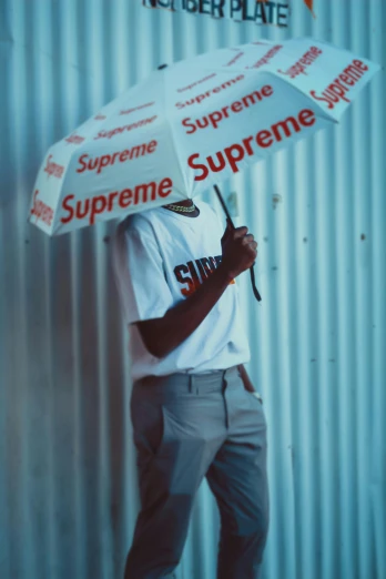 a man standing in front of a wall holding an umbrella, inspired by Bert Stern, unsplash, supreme, playboi carti, * * * * *, sup